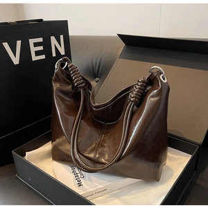 Detail of a dark brown glossy leather tote bag with thick rope knot handles in a luxury gift box