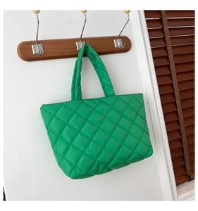 Close-up of a green quilted puffer tote bag hanging on a wooden hook in a modern room