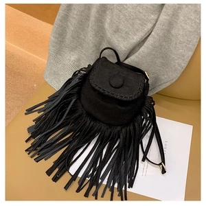 Detail of a black suede crossbody bag with long fringes on a soft couch background