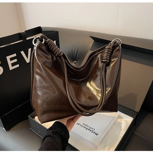 Detail of dark brown tote bag featuring unique spiral knot handle and silver metal rings
