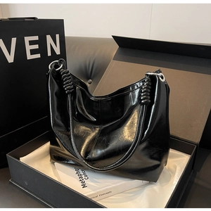 Detail of black glossy leather tote bag with knot shoulder strap and silver ring in gift box