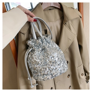 Gros plan d'un sac seau à paillettes argentées devant un trench-coat beige élégant