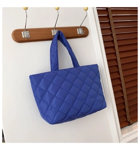Close-up of royal blue quilted tote bag with diamond pattern on a wooden hanger