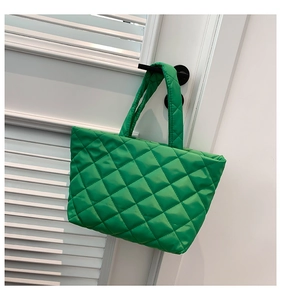 Detail of green quilted puffer tote bag with diamond stitching hanging on door handle