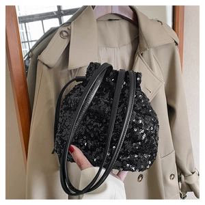 Détail d'un sac seau noir à paillettes avec cordon de serrage tenu sur un trench