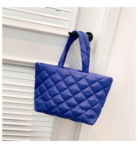 Royal blue quilted tote bag with diamond stitching hanging on a white shutter door