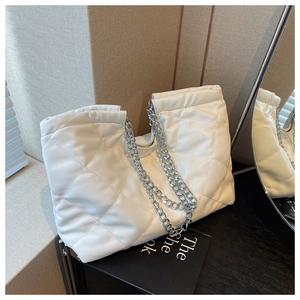 Detailed view of white quilted faux leather texture and silver chain strap on tote bag