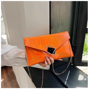 Detail of bright orange envelope clutch with crocodile texture and gold chain strap