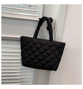Detail of black quilted puffer tote bag with classic diamond stitch texture and soft handle