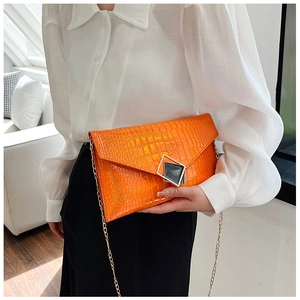 Detail view of the bright orange envelope clutch bag with crocodile texture and gold chain