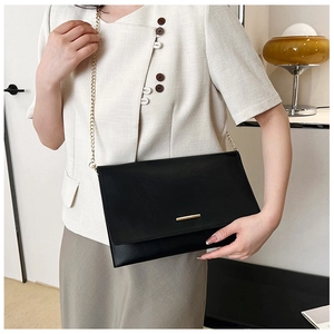 Detail of a black leather flap bag with gold chain strap shown on a model