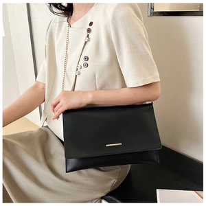 Minimalist black envelope crossbody bag with gold metal trim shown on model