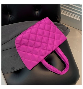 Macro view of magenta quilted tote bag with padded texture on a grey suit background