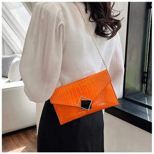 Close-up of bright orange envelope clutch featuring crocodile texture and gold chain strap