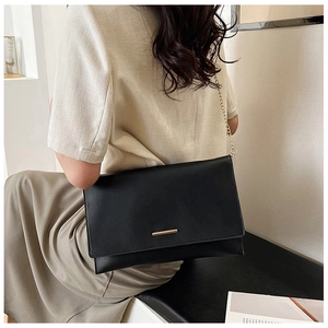 Detail of a black envelope crossbody bag with a gold metal bar and chain strap for women