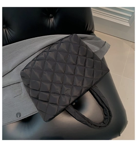 Close-up of black quilted puffer tote bag placed on a leather chair with a gray blazer