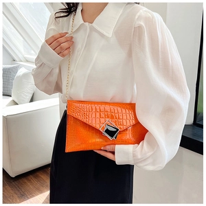 Detail of orange crocodile pattern envelope bag with silver metallic buckle and gold chain