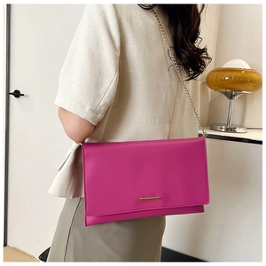 Detail view of the magenta envelope bag with a sleek gold metal bar and chain strap