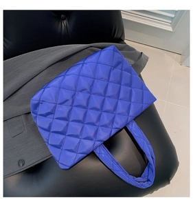 Detail of royal blue quilted tote bag with soft padded handle on black background