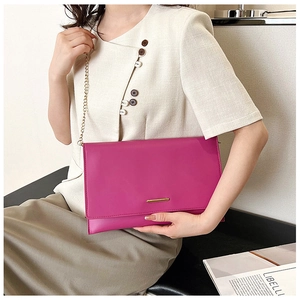 Detail of hot pink envelope bag with gold metal trim and chain strap shown with outfit