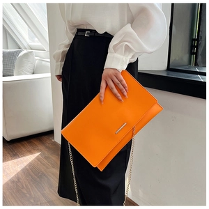 Detail of orange envelope clutch featuring metal trim and elegant gold chain strap