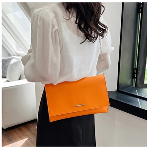 Luminous orange geometric envelope bag with gold chain strap shown on a model
