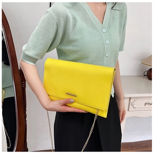 Detailed view of bright yellow geometric envelope bag with gold chain strap and metal buckle