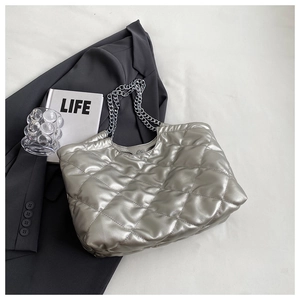 Close-up of metallic silver quilted chain tote bag on a professional grey blazer background