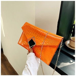 Detail of orange crocodile texture envelope clutch with gold geometric buckle and chain