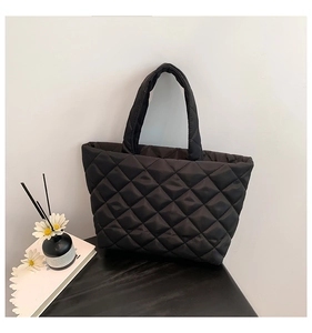 Close-up of black quilted puffer tote bag with diamond texture on a modern desk