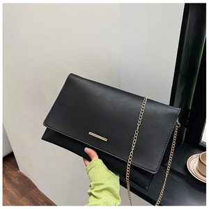 Detail of minimalist black matte clutch featuring a sleek gold metal bar and chain strap