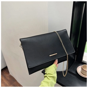 Close-up of a black geometric envelope clutch bag with gold bar and metal chain strap