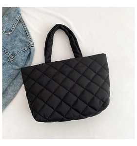 Detail shot of black quilted tote bag with diamond stitching on soft white fabric