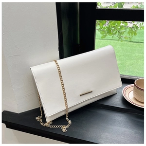 Close-up of a white matte leather envelope bag with gold chain strap on a window sill
