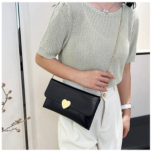 Detail of a black leather envelope bag with a gold heart-shaped metal buckle and chain