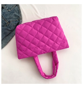 Flat lay of a fuchsia quilted puffer tote bag next to denim on white background