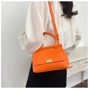 Detail of orange lychee texture handbag featuring a gold buckle and adjustable strap