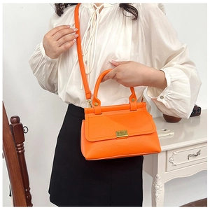 Detail of orange litchi grain shoulder bag with golden buckle and slim strap on model