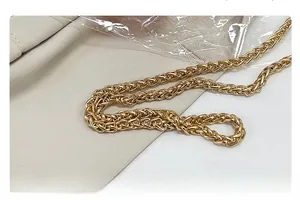 Détail d'une bandoulière en chaîne dorée tressée avec une texture fine façon épi de blé