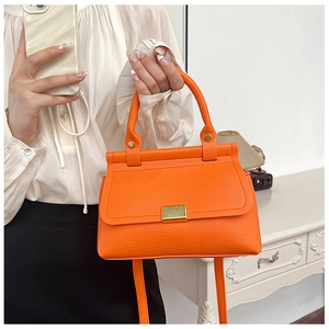 Close-up of bright orange lychee textured handbag with gold metal lock and leather handle