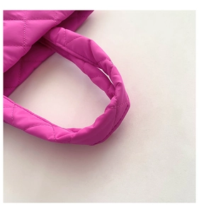 Macro detail of rose red quilted nylon tote bag featuring thick padded handles