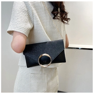Detail of black glitter envelope clutch featuring a large gold ring buckle and chain strap