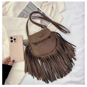 Close-up of brown suede saddle bag with fringe details and woven edges with a phone for scale