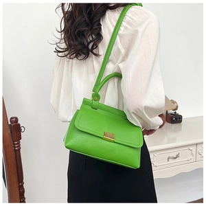 Detail of neon green lychee pattern handbag with gold clasp worn by a model