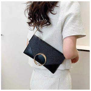 Detail of black envelope clutch featuring a gold ring buckle and metallic chain strap