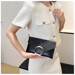 Detail of black envelope clutch with gold ring buckle and chain strap on a model