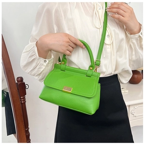 Detail of green litchi grain leather bag with gold buckle and top handle worn by model
