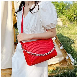 Detail of red pleated crossbody bag with silver chain strap shown in outdoor setting