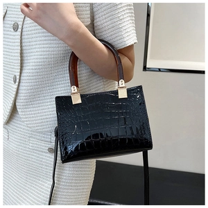 Detail of black glossy crocodile texture handbag with amber handle and gold hardware