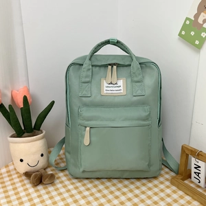Close-up of mint green casual backpack featuring front zipper pocket and white square label